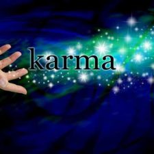 Female hand outstretched with the word 'Karma' floating away amongst a stream of sparkles on a dark blue swirling background with a swirl of green light behind the glitter